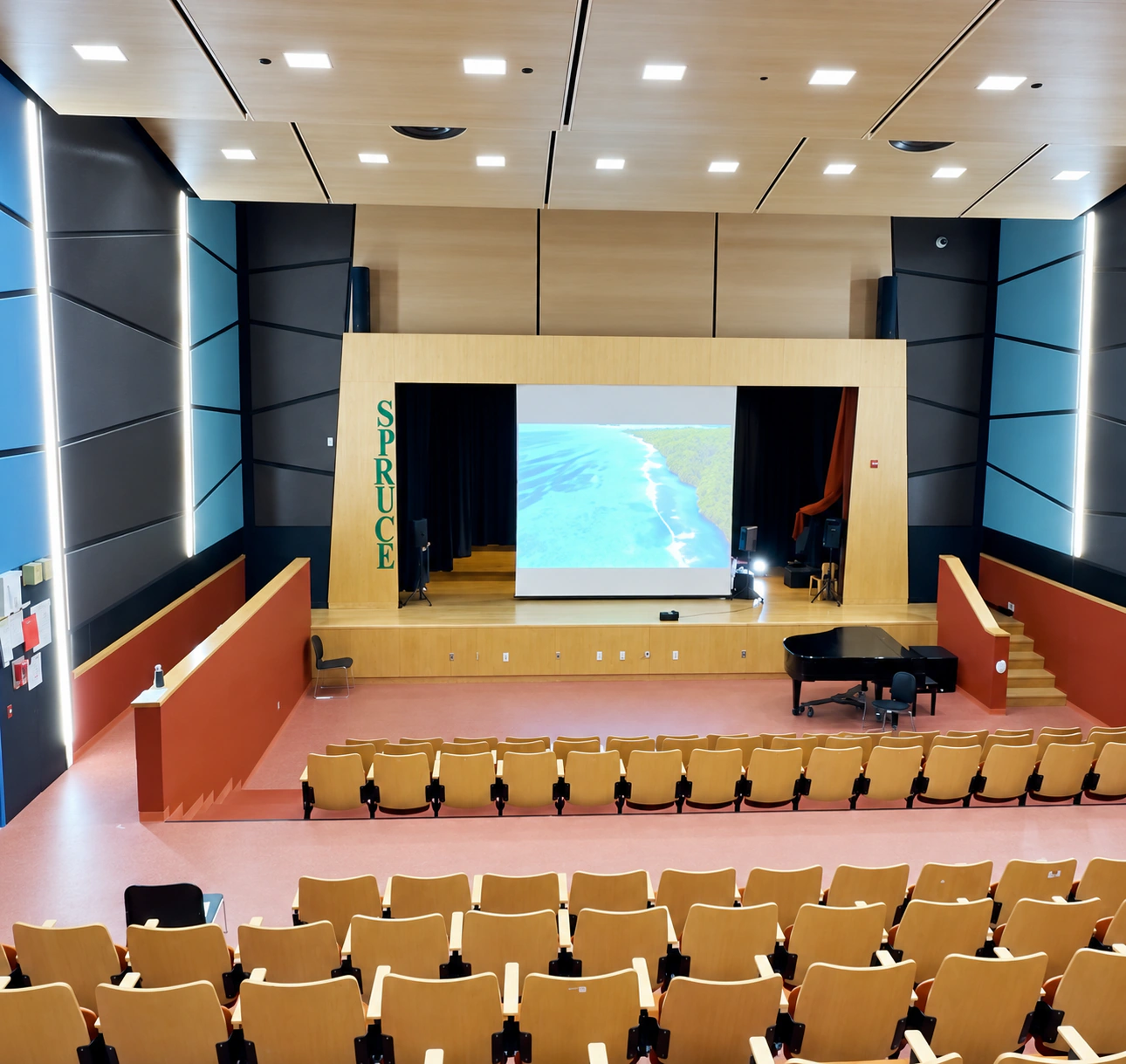 School auditorium with stage, projection screen, acoustic panels and seating
