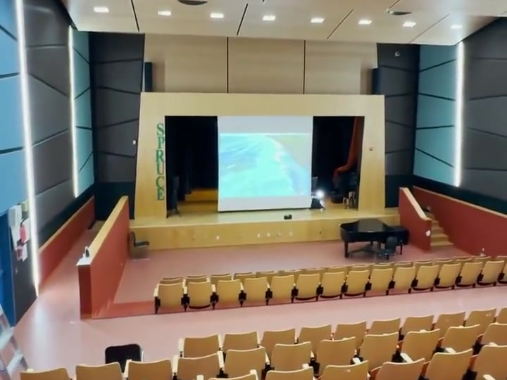 Wide stage, operating projection screen, piano and auditorium seating.